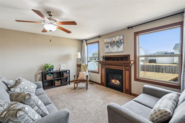 living area with visible vents, a textured ceiling, a glass covered fireplace, carpet floors, and baseboards