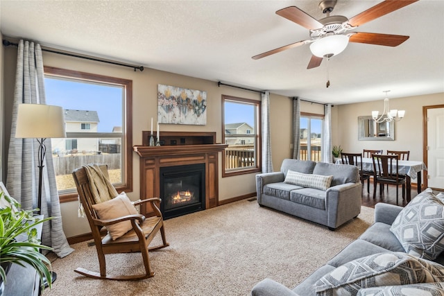 living room with ceiling fan with notable chandelier, a textured ceiling, a glass covered fireplace, carpet floors, and baseboards