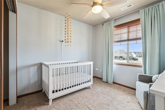 bedroom with visible vents, a crib, carpet, baseboards, and a ceiling fan