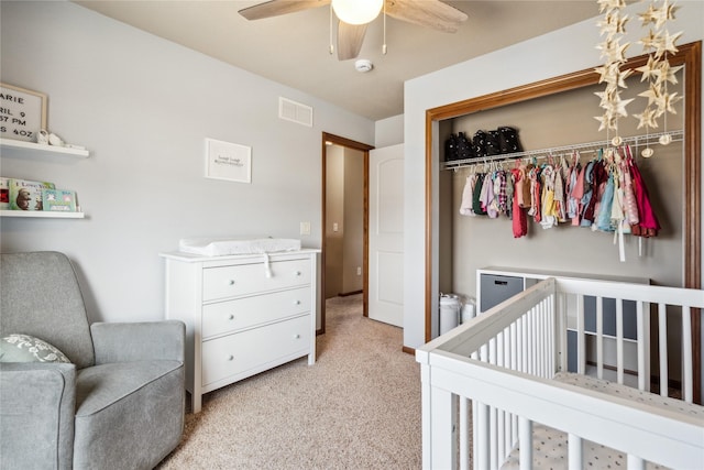 bedroom with a ceiling fan, visible vents, a nursery area, a closet, and light carpet