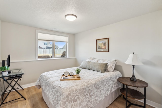 bedroom featuring visible vents, a textured ceiling, baseboards, and wood finished floors