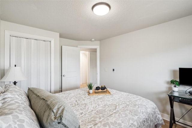 bedroom featuring a closet, a textured ceiling, baseboards, and wood finished floors