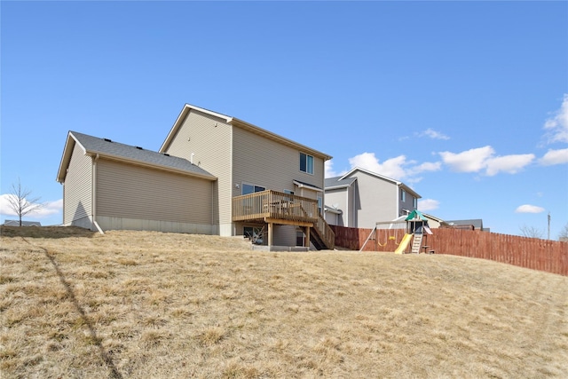 rear view of property with a wooden deck, a playground, and fence