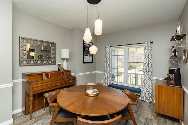 dining space with a textured ceiling, baseboards, and wood finished floors