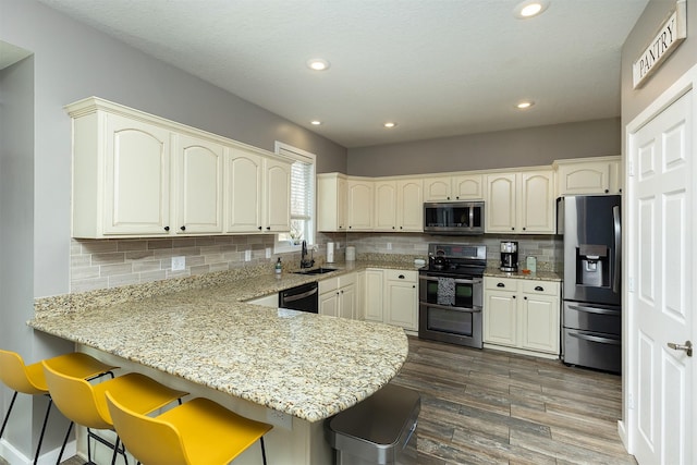 kitchen with light stone countertops, decorative backsplash, appliances with stainless steel finishes, a peninsula, and a sink