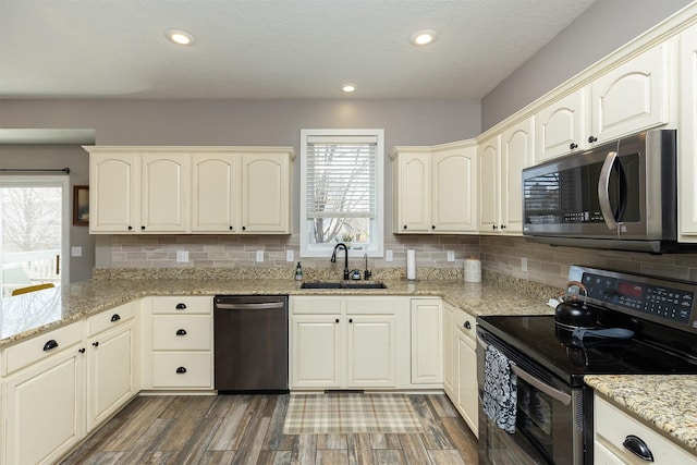 kitchen featuring tasteful backsplash, light stone counters, appliances with stainless steel finishes, wood finished floors, and a sink