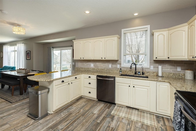 kitchen featuring wood finished floors, a peninsula, a sink, dishwasher, and backsplash