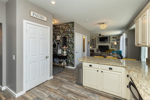 kitchen with baseboards, a peninsula, light wood-style flooring, a fireplace, and open floor plan