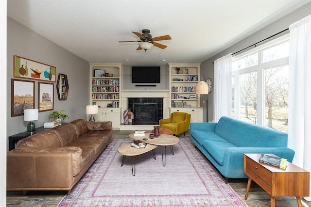 living area featuring built in features, a tile fireplace, a ceiling fan, and wood finished floors