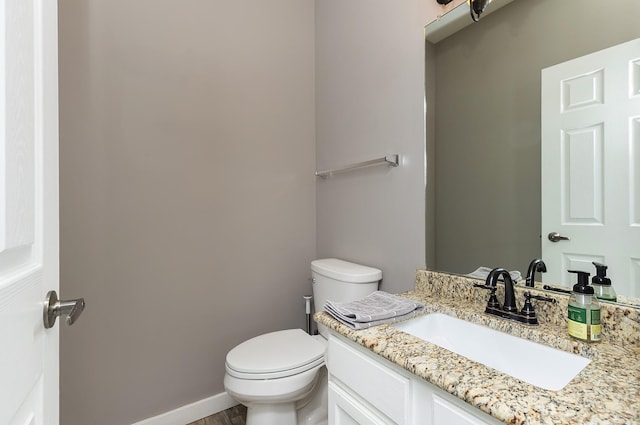 half bathroom with vanity, toilet, and baseboards