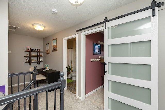 interior space with a barn door, light colored carpet, baseboards, and a textured ceiling