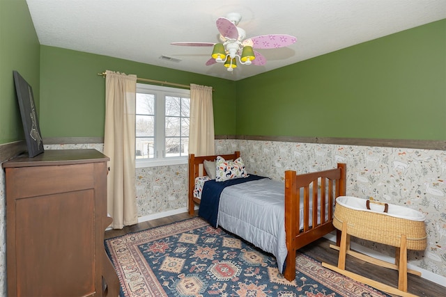 bedroom featuring visible vents, wood finished floors, a wainscoted wall, and wallpapered walls