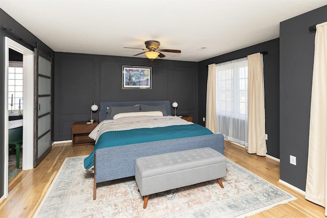 bedroom with baseboards, light wood-style flooring, a ceiling fan, and a decorative wall