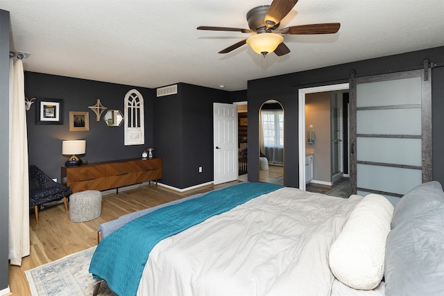 bedroom with wood finished floors, visible vents, baseboards, a textured ceiling, and a barn door