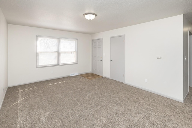 carpeted empty room with visible vents, a textured ceiling, and baseboards