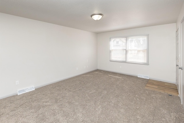 carpeted spare room featuring visible vents, a textured ceiling, and baseboards