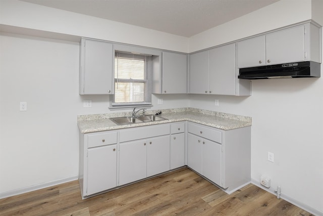 kitchen with under cabinet range hood, light wood finished floors, light countertops, and a sink