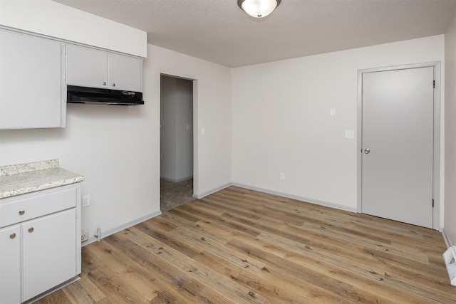 kitchen with under cabinet range hood, a textured ceiling, light wood finished floors, baseboards, and light countertops