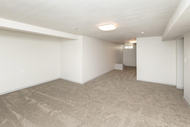 below grade area featuring light carpet, a textured ceiling, and baseboards