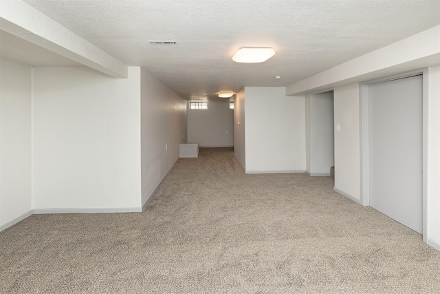 basement featuring a textured ceiling, baseboards, visible vents, and light carpet