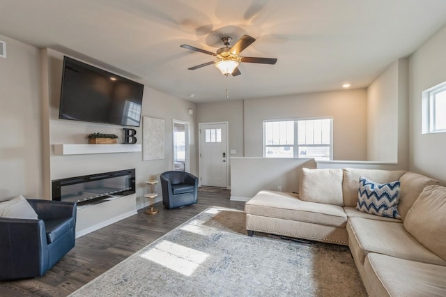 living room with baseboards, dark wood-type flooring, a healthy amount of sunlight, and a glass covered fireplace