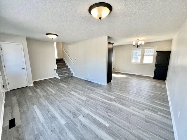 unfurnished living room featuring stairway, wood finished floors, visible vents, and baseboards