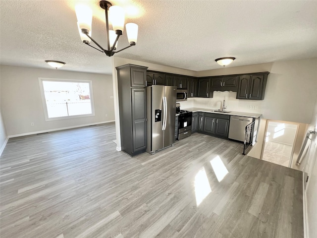 kitchen with a sink, stainless steel appliances, light wood-style floors, light countertops, and a chandelier