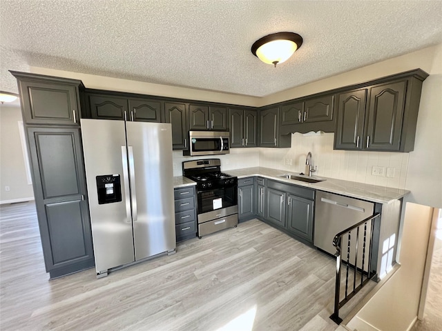 kitchen featuring light wood-style flooring, a sink, stainless steel appliances, light countertops, and a textured ceiling