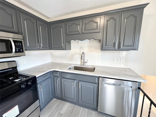 kitchen featuring light stone countertops, light wood-style floors, appliances with stainless steel finishes, and a sink