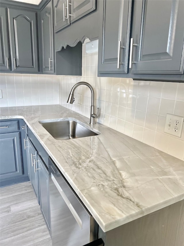 kitchen featuring light stone counters, a sink, decorative backsplash, light wood-style floors, and dishwasher