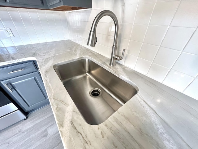 interior details featuring backsplash, light stone countertops, wood finished floors, blue cabinets, and a sink