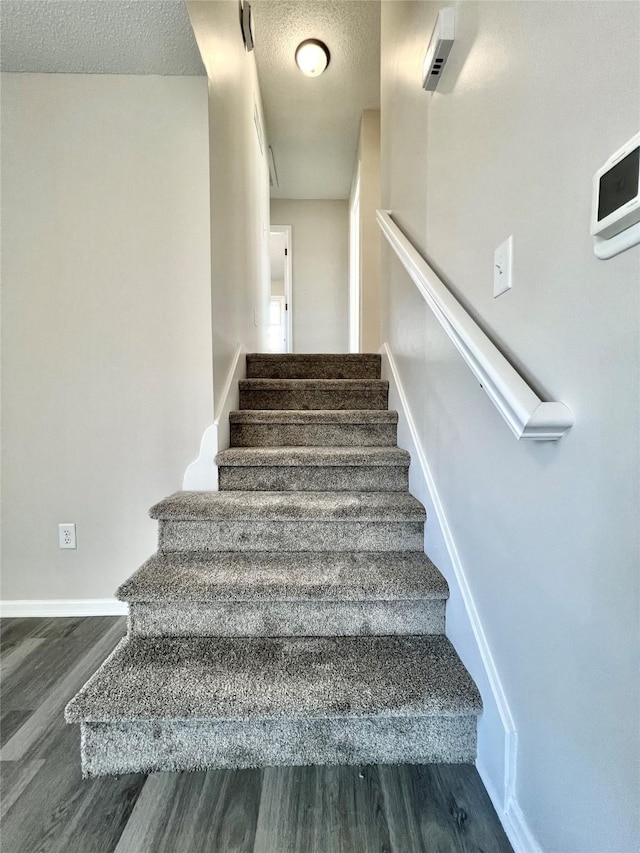 staircase with a textured ceiling, baseboards, and wood finished floors