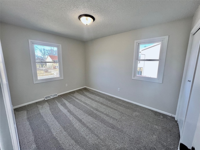 unfurnished bedroom featuring dark colored carpet, visible vents, multiple windows, and baseboards