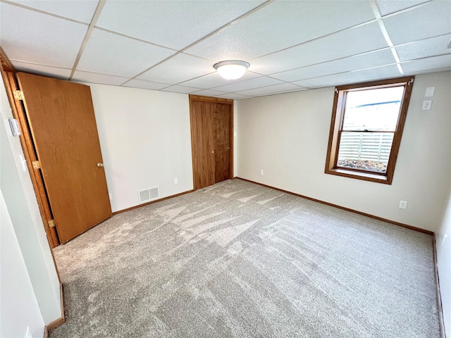 carpeted spare room featuring baseboards, visible vents, and a drop ceiling