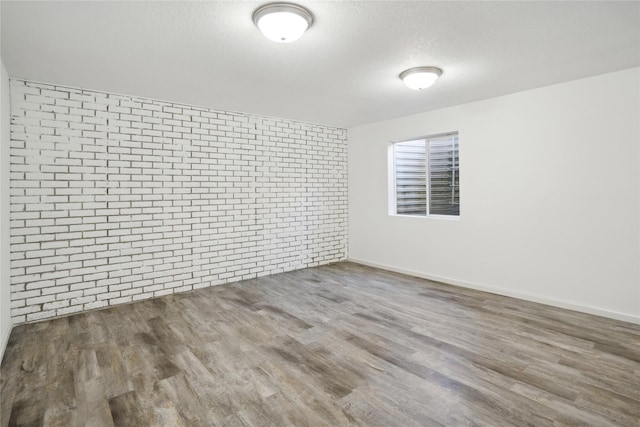 empty room with wood finished floors, baseboards, brick wall, and a textured ceiling