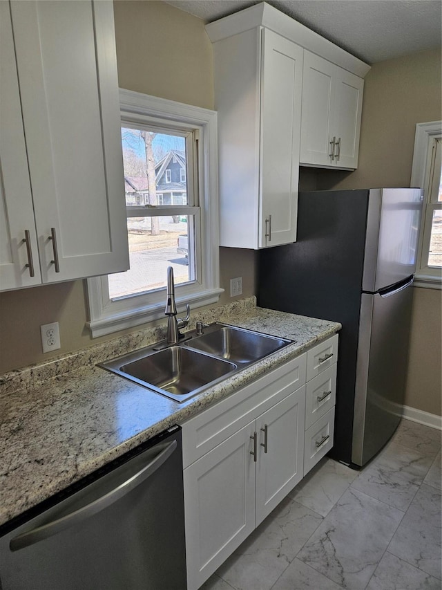 kitchen featuring baseboards, white cabinets, marble finish floor, stainless steel appliances, and a sink