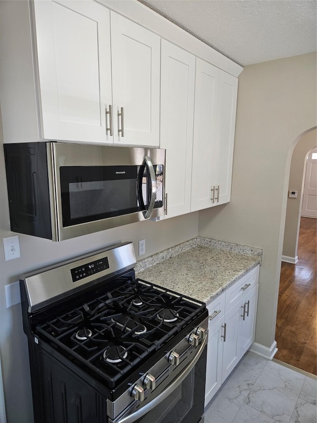 kitchen featuring baseboards, arched walkways, stainless steel appliances, white cabinetry, and marble finish floor