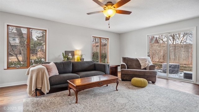 living room with a ceiling fan, wood finished floors, baseboards, and a textured ceiling