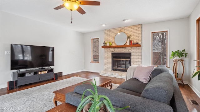 living room featuring visible vents, a brick fireplace, baseboards, wood finished floors, and a ceiling fan