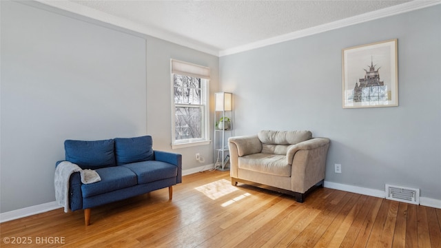 sitting room with baseboards, visible vents, light wood finished floors, and ornamental molding