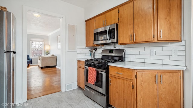 kitchen with visible vents, tasteful backsplash, stainless steel appliances, brown cabinetry, and light countertops