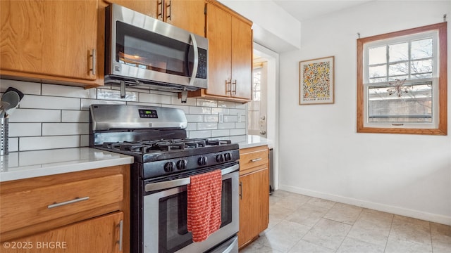 kitchen with backsplash, appliances with stainless steel finishes, brown cabinetry, light countertops, and baseboards