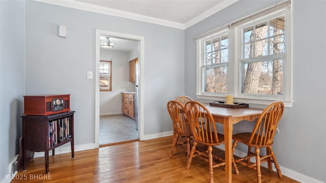 dining space featuring visible vents, light wood-style floors, baseboards, and ornamental molding