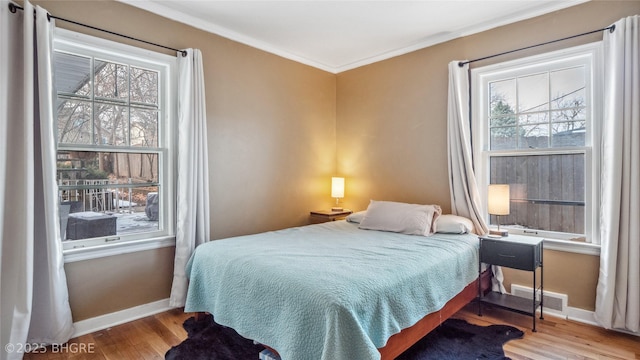 bedroom with crown molding, multiple windows, wood finished floors, and baseboards