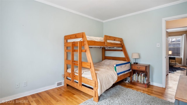 bedroom with visible vents, ornamental molding, baseboards, and wood finished floors