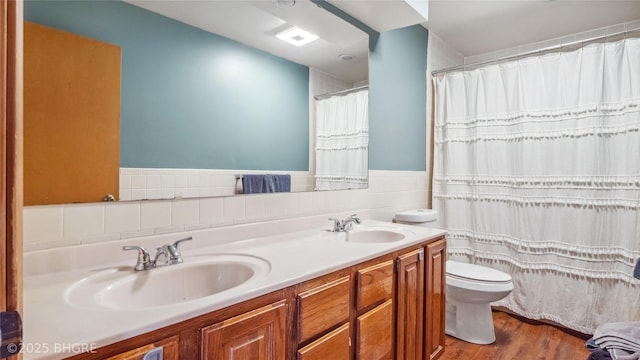 full bathroom with a wainscoted wall, toilet, tile walls, and a sink