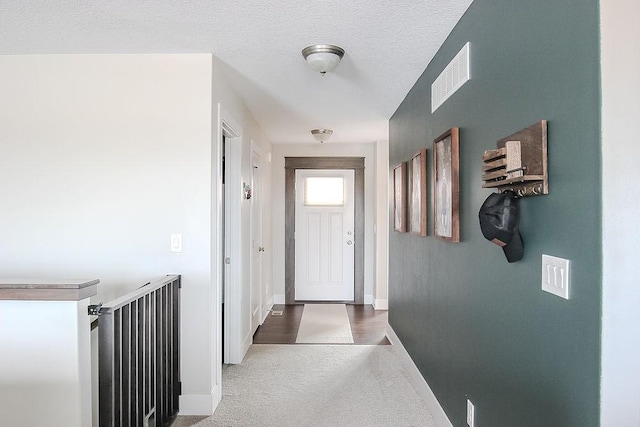 hallway with visible vents, a textured ceiling, baseboards, and carpet floors