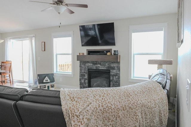 living room featuring a stone fireplace, ceiling fan, and a healthy amount of sunlight