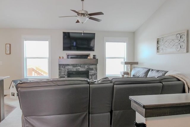 living area featuring plenty of natural light, a stone fireplace, a ceiling fan, and vaulted ceiling