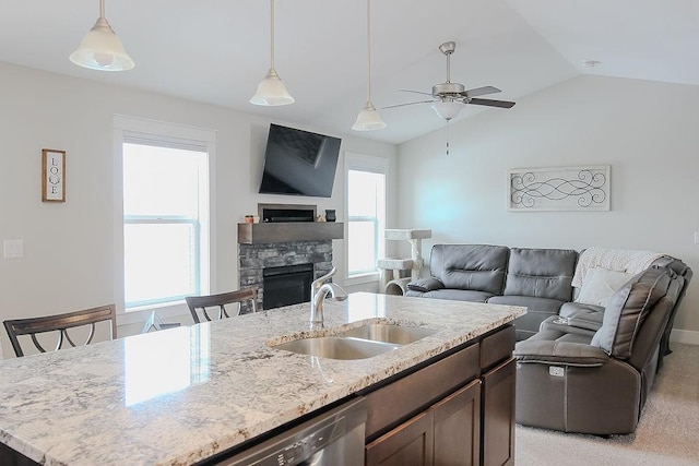 kitchen with a center island with sink, a sink, a stone fireplace, pendant lighting, and open floor plan